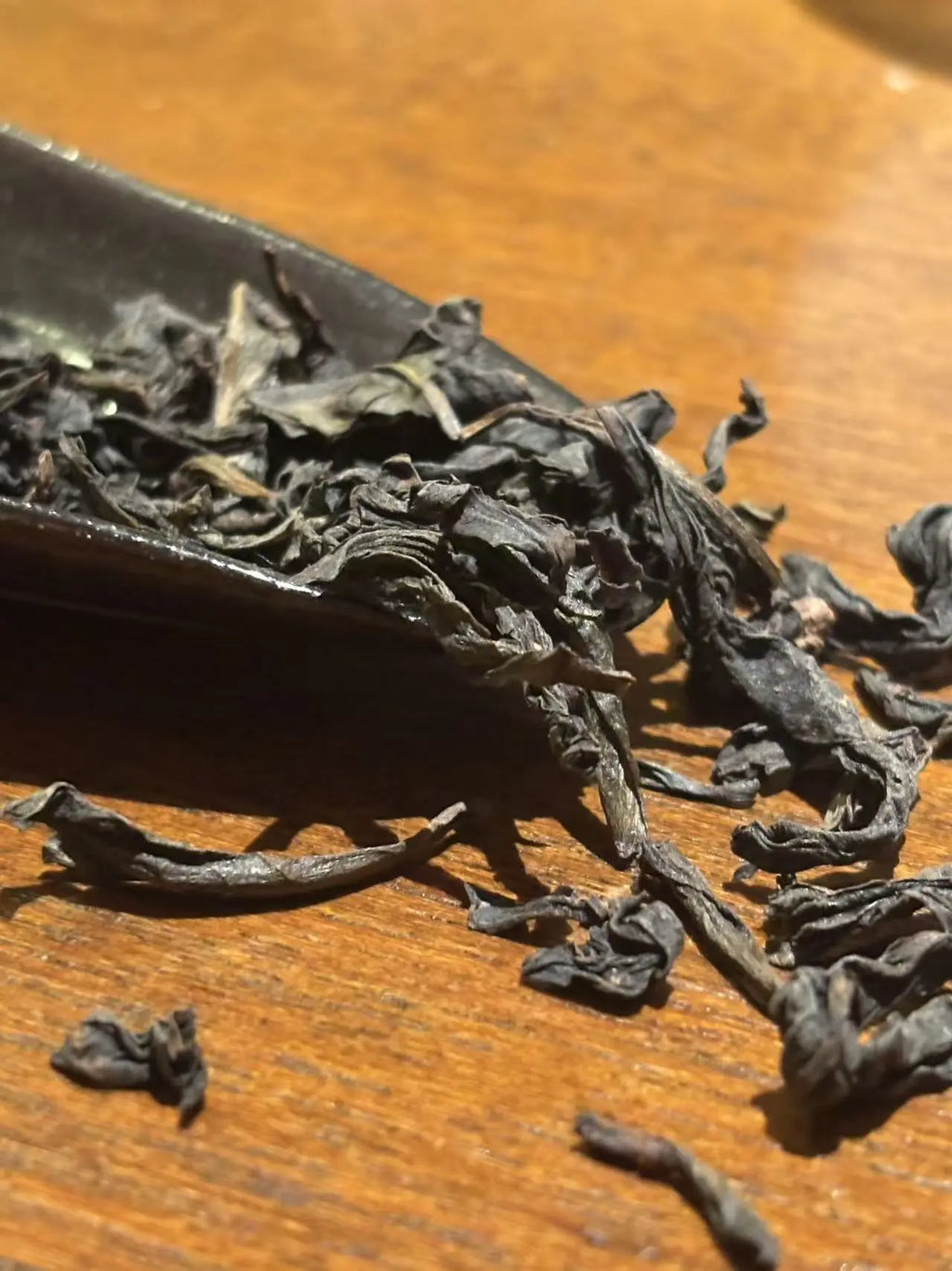 Close-up of Jin Jun Mei loose-leaf tea leaves spilling from a dark scoop onto a warm wooden surface.