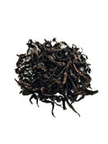 A pile of dark, dried loose-leaf Cinnamon Rock tea leaves on a clean white background.