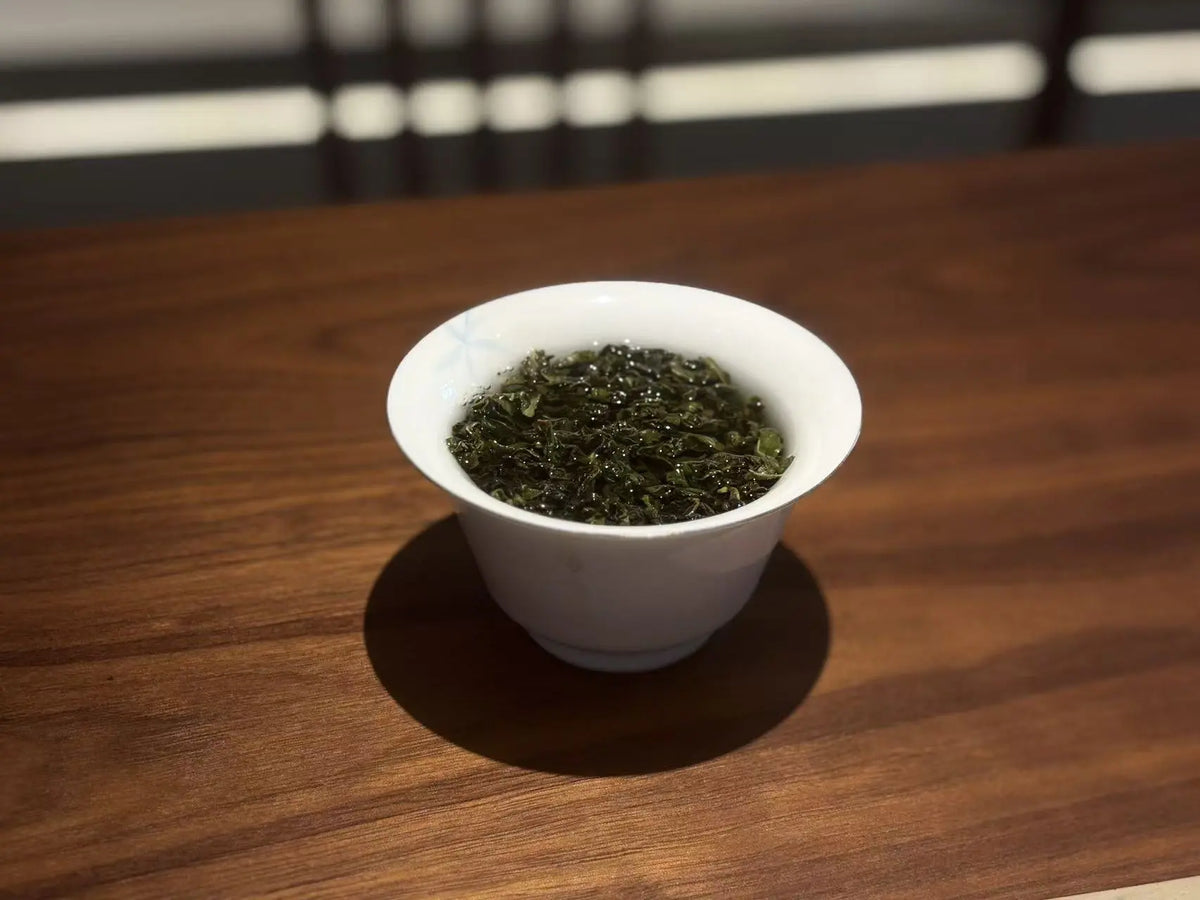 A white ceramic tea bowl filled with brewed green tea, set on a polished wooden table.