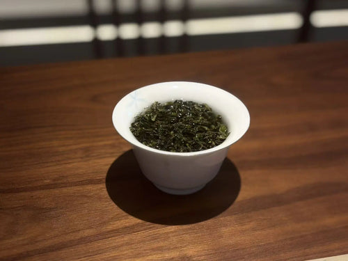 A white ceramic tea bowl filled with brewed green tea, set on a polished wooden table.