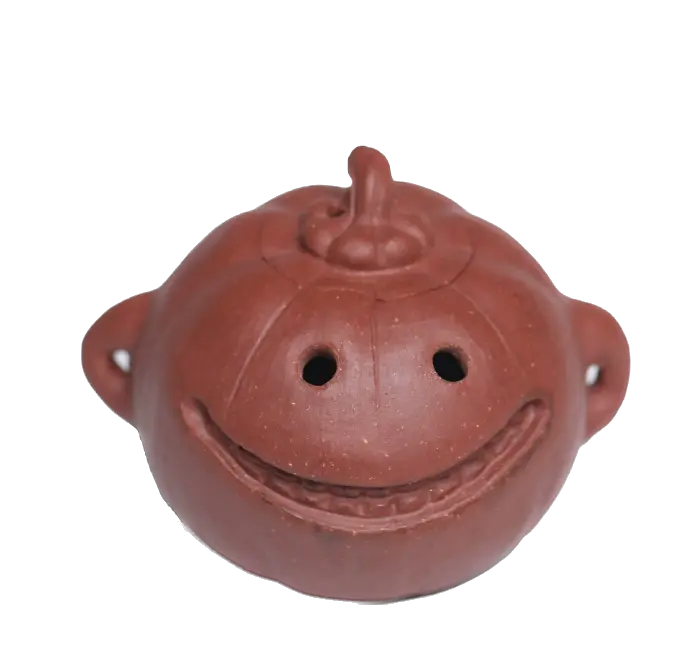 A small reddish-brown ceramic pumpkin-shaped vessel with a smiling face, photographed on a plain white background.