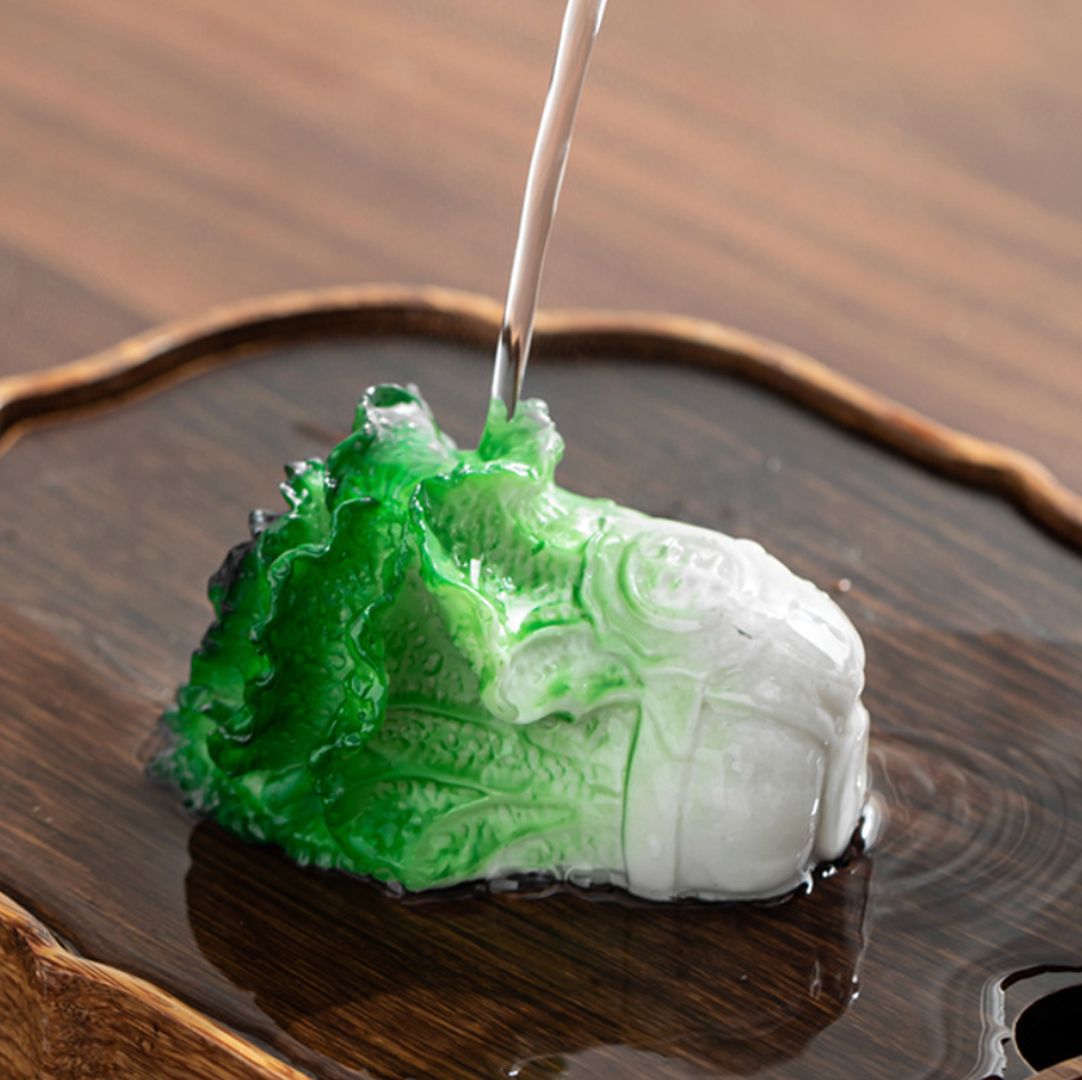 A close up shot of a jade-like cabbage lying on a wooden tea tray,  A jet of water is spraying upwards.