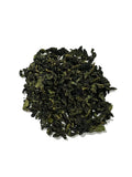 A small pile of dark green loose-leaf tea on a plain white background.
