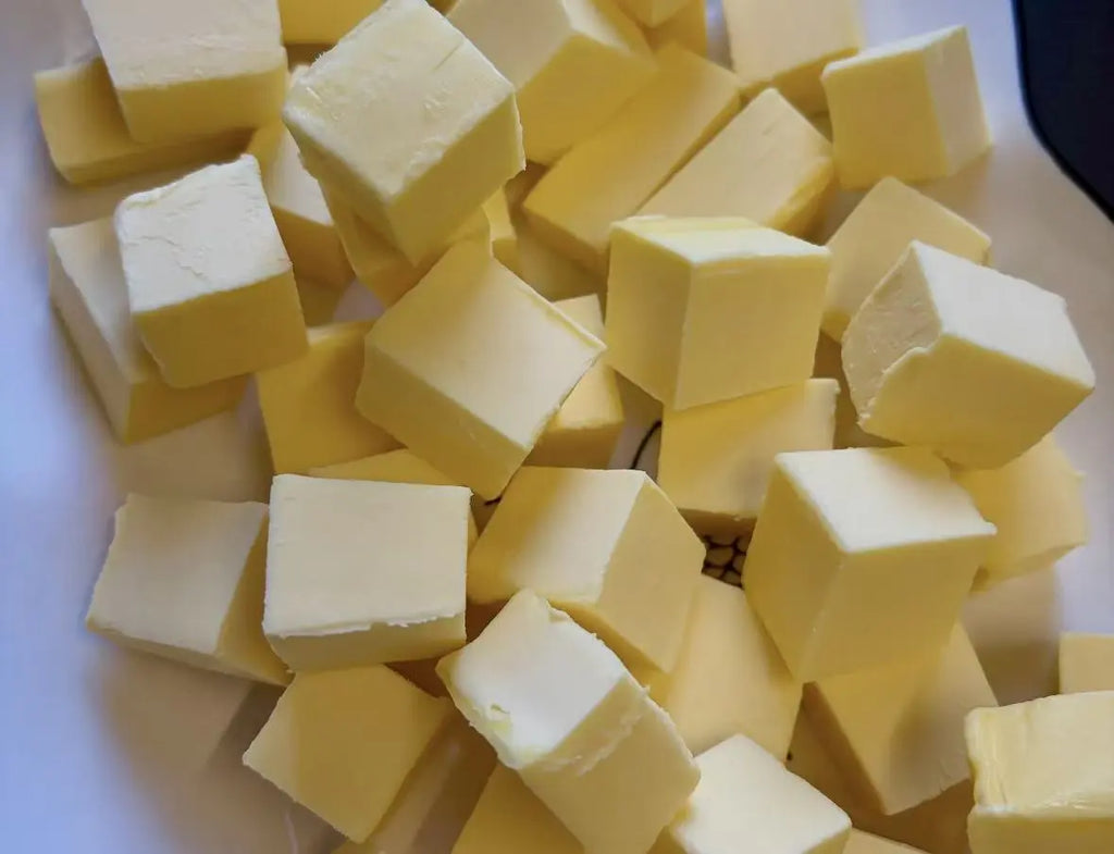 A pile of cubed butter pieces in pale yellow, photographed close-up on a white surface. The tea liquor has a smooth butter taste 